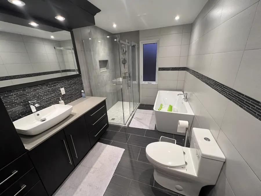 Salle de bain avec vasque, vanité noire, douche vitrée et bain