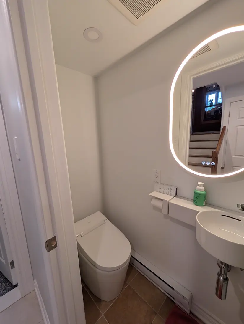 Salle d'eau avec toilette, petit lavabo et miroir rétroéclairé arrondi