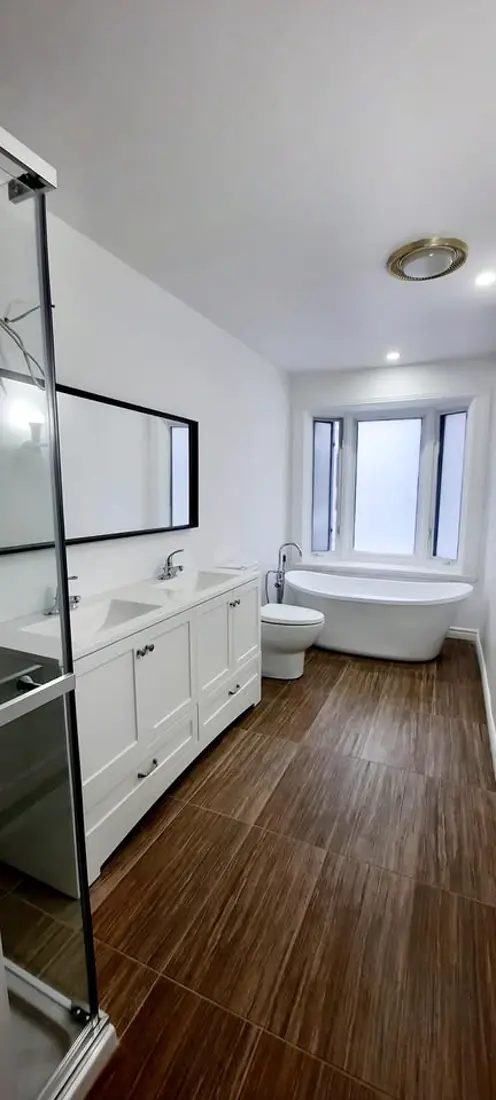 Grande salle de bain avec double vanité blanche, plancher bois et bain autoportant